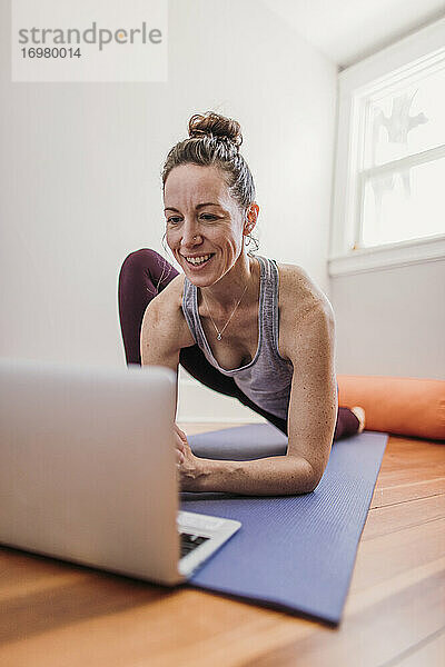 Frau lächelt  während sie zu Hause am Computer Yoga übt