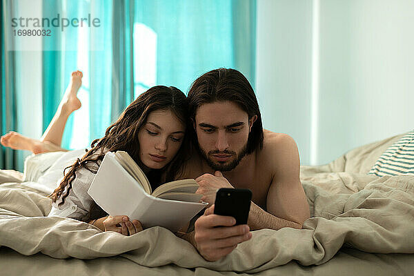 Junger Mann schaut auf sein Smartphone  während seine Freundin Boo liest