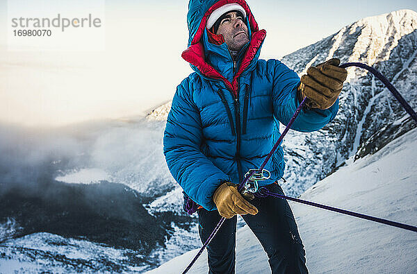 Männlicher Kletterer sichert seinen Vorsteiger bei einer kalten alpinen Wintertour