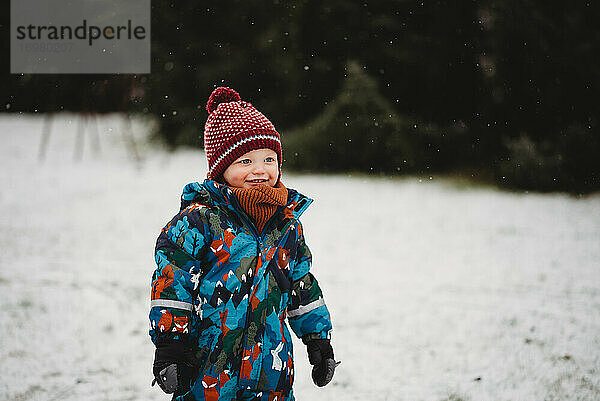 Schöner Junge lächelnd draußen im Park auf kalten verschneiten Tag im Winter