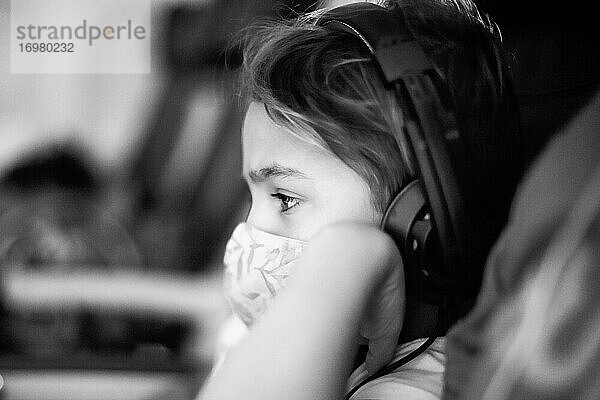 Kind in einem Flugzeug mit Kopfhörern und Maske.