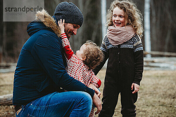 Vater lächelt und umarmt Kinder im Wald im Winter in Norwegen