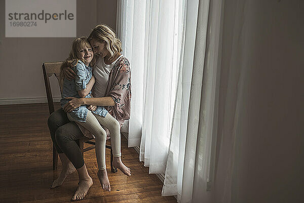 Mutter und Tochter sitzen eng beieinander am Fenster im Atelier