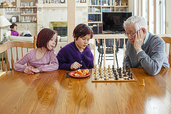 Zwei Kinder spielen Schach mit Großvater und Frau liest im Hintergrund