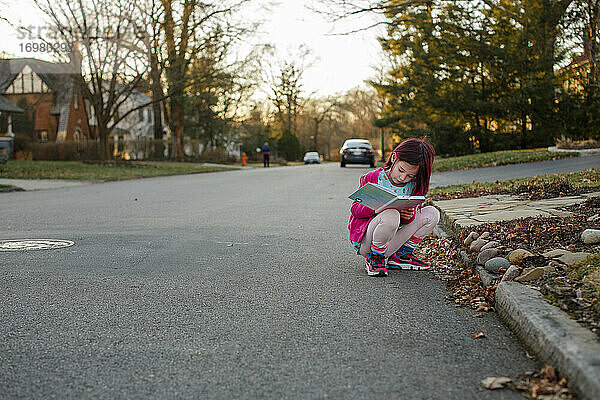Kleines Mädchen hockt auf der Straße  um bei Sonnenuntergang Notizen in ein Tagebuch zu schreiben
