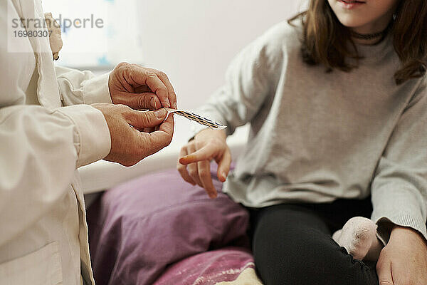 Nahaufnahme einer Ärztin  die einem Mädchen im Bett ein Pflaster auf den Finger klebt. Hausarzt-Konzept