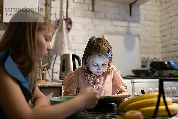 Mädchen spielt Spiel auf Tablet in der Nähe von Essen Schwester