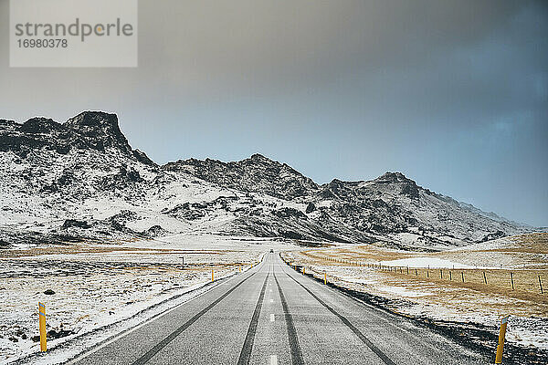 Verschneite Straße und Berge an einem bedeckten Tag