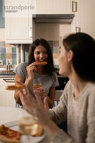 Junge Frau beißt in eine Pizza und hört einem Freund zu
