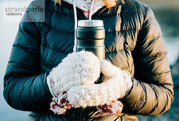Frau mit Händen in traditionellen nordischen Handschuhen hält ein heißes Getränk