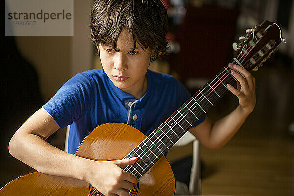 Nahaufnahme eines konzentrierten Jungen  der im Fensterlicht klassische Gitarre übt