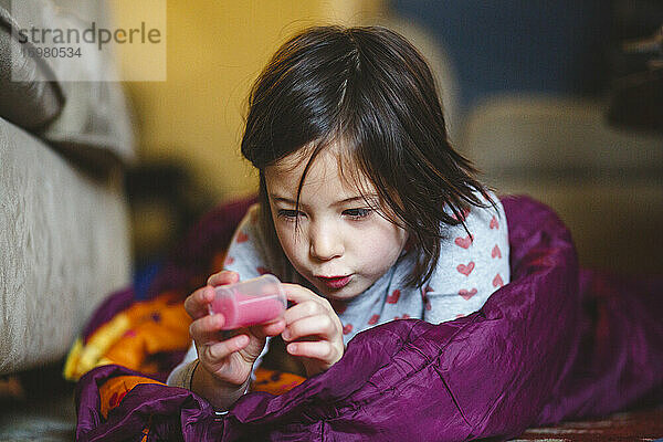 Ein kleines Mädchen liegt in einem Schlafsack auf dem Boden und studiert eine Tube mit Flüssigkeit