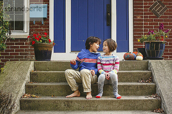 Ein Bruder und eine Schwester sitzen lächelnd auf der Eingangstreppe ihres Hauses