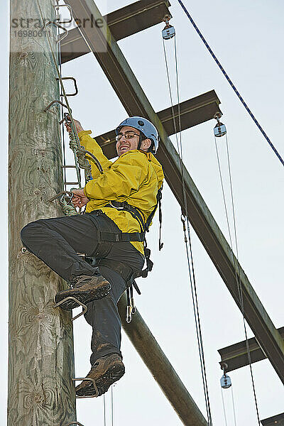 Mann klettert bei einer Hochseilübung auf eine Holzstange