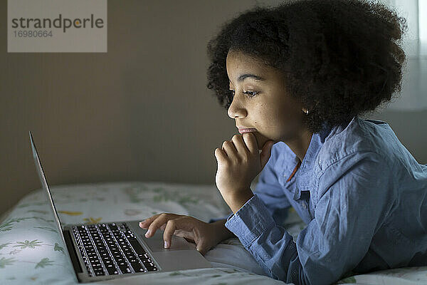 Seitenansicht eines zehnjährigen gemischtrassigen Mädchens bei der Arbeit an ihrem Laptop