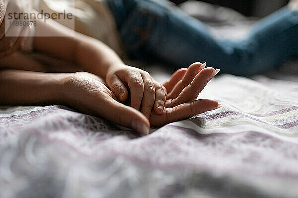 Abgeschnittene Mutter und Kind halten sich auf dem Bett an den Händen