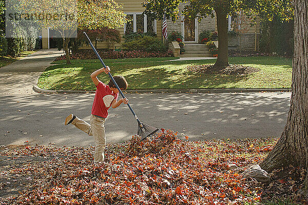 ein Junge harkt an einem warmen Herbsttag draußen mit Begeisterung Blätter zusammen