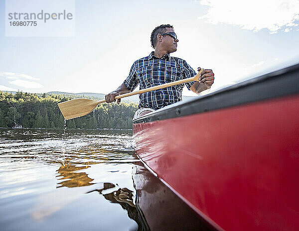 Afroamerikanischer Mann paddelt mit einem roten Kanu auf einem friedlichen See in Maine