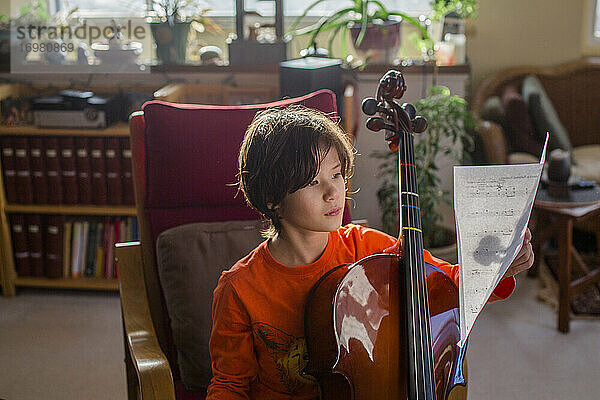 Ein Junge sitzt in schönem Licht mit einem Cello und liest Noten