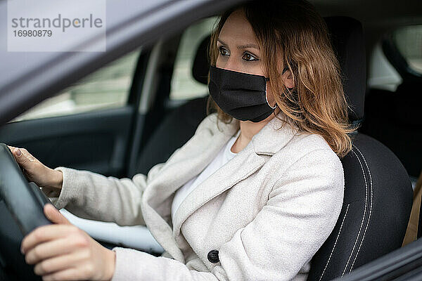 Frau mit Schutzmaske fährt Auto