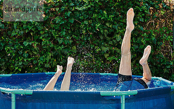 Die Beine von zwei Personen  die in ein häusliches Schwimmbad im Garten springen.