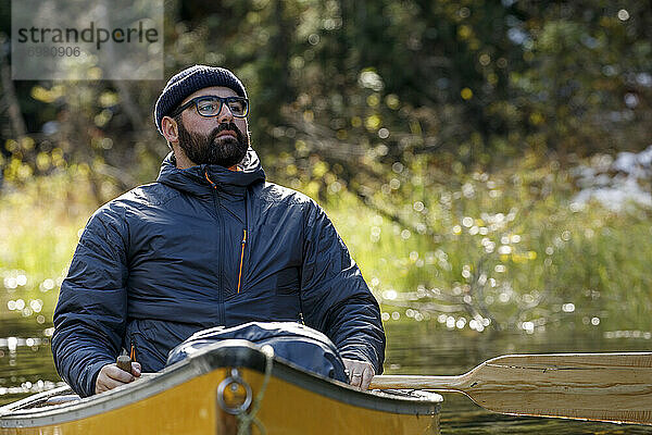 Ein aufrichtiger Mann sitzt im Kanu auf einem ruhigen See und genießt die Natur