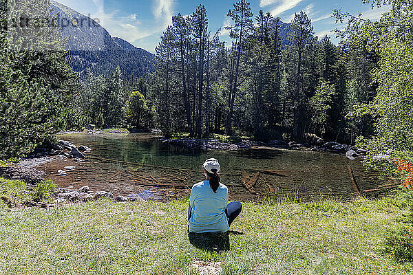 Frau mittleren Alters sitzt an einem transparenten Bergsee und schaut in die Landschaft  Pyrenäen