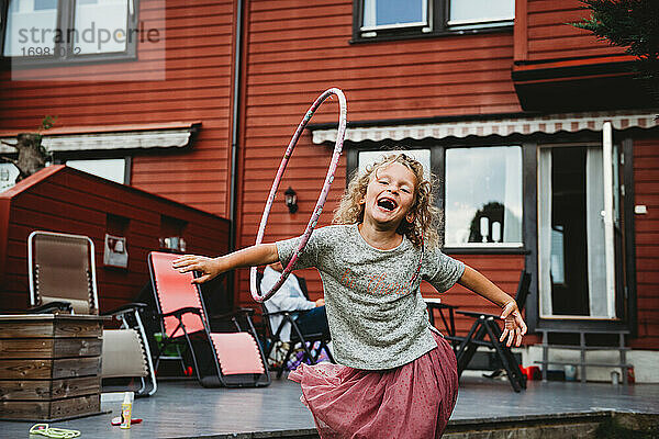 Nettes Mädchen hat Spaß mit Hula-Hoop-Reifen im Hinterhof mit roten Holzhaus