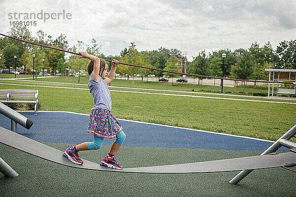 Ein kleines Mädchen balanciert im Sommer draußen auf einem Spielplatzgerät