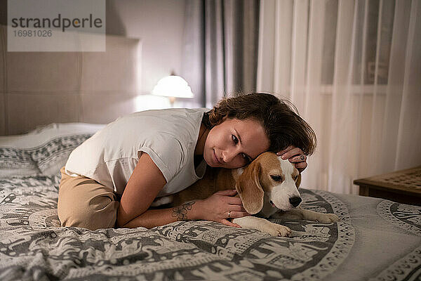 Junge Frau  die ihren Hund auf dem Bett umarmt