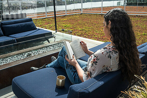 Frau sitzt auf einem Dach im Freien und liest ein Buch an einem sonnigen Tag