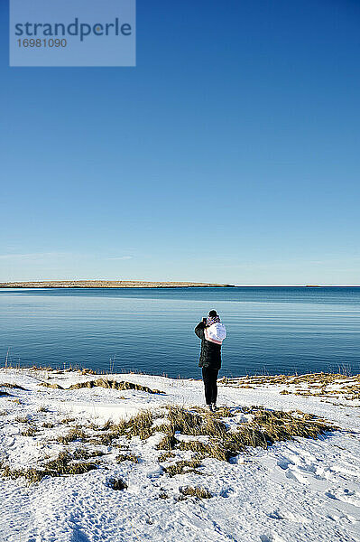 Anonyme Frau entspannt sich am verschneiten Meeresufer an einem sonnigen Tag