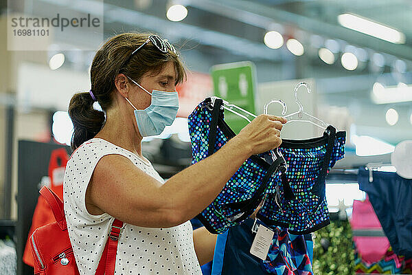 Frau mit medizinischer Maske bei der Kleiderauswahl in einem Einkaufszentrum