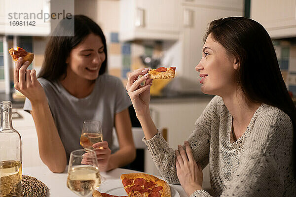 Glückliche junge Frauen mit Pizza im Gespräch in der Küche