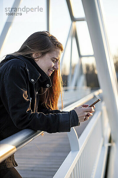 junge erwachsene Frau  die auf einem Steg mit ihrem Telefon lacht