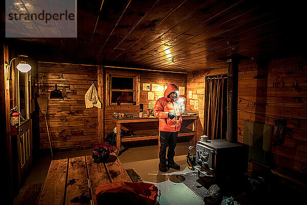Ein Mann steht in einer kalten Hütte und wartet darauf  dass das Feuer wärmt