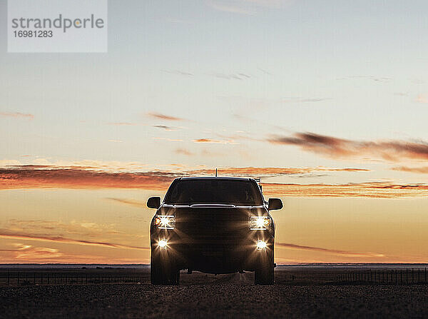 Silhouette eines Lastwagens bei Sonnenaufgang mit eingeschalteten Scheinwerfern und Nebelscheinwerfern