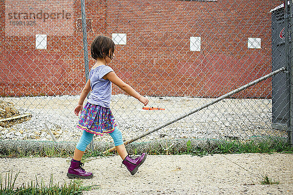 Ein kühnes Mädchen in lila Stiefeln läuft auf dem Bürgersteig neben einer Baustelle
