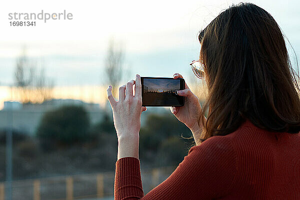 Junge Frau macht ein Foto mit ihrem Handy bei Sonnenuntergang