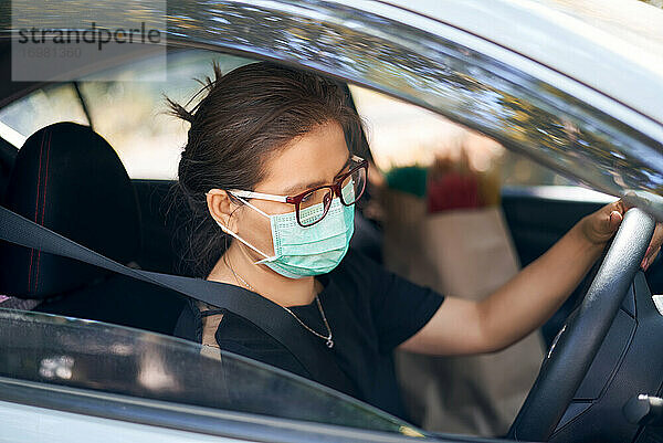 Frau trägt eine chirurgische Maske und fährt ein Auto während des Covid-19