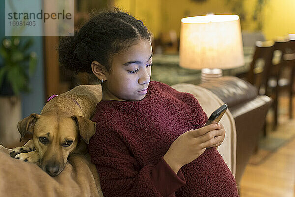 Biracial tween Blick auf Telefon  während lehnt sich gegen kleine braune Hund