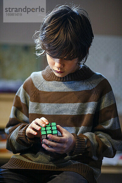 Ein kleiner Junge im übergroßen Pullover löst geduldig einen Rubik's Cube
