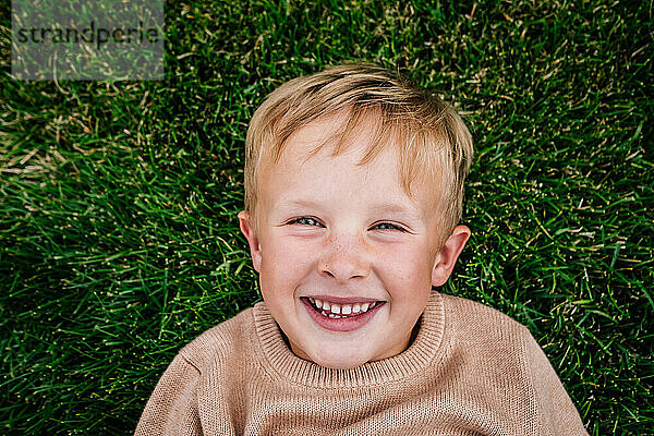 Glücklicher Junge liegt lächelnd im Gras