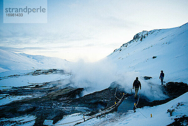 Zwei Menschen gehen an geothermischen Becken vorbei zum Fluss Reykjadalur