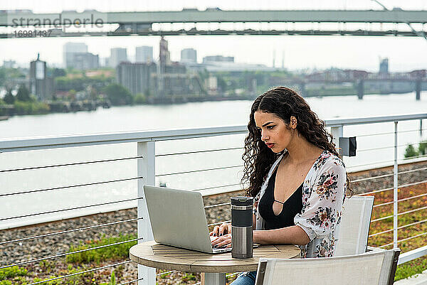 Frau arbeitet am Laptop an einem kleinen Tisch draußen auf dem Dach