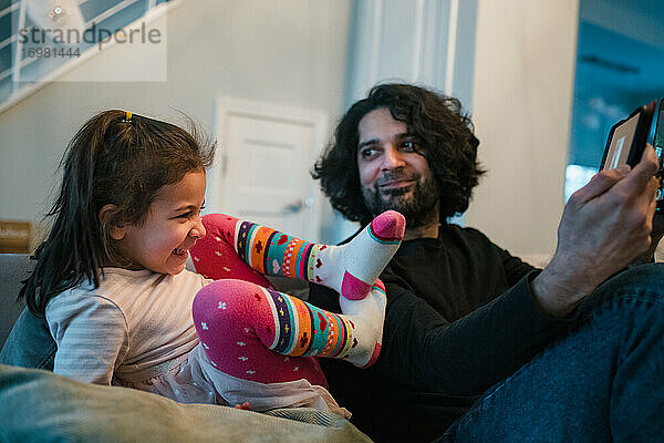 Vater und Tochter spielen zusammen auf dem iPad und lachen