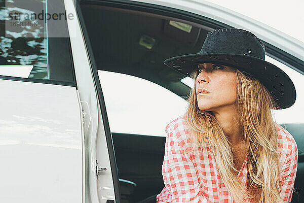 Attraktive Frau mit Cowgirl-Hut  die in der Tür eines weißen Autos sitzt