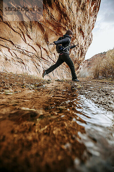 Wanderin springt beim Wandern im Canyon über einen Bach  Boulder Utah