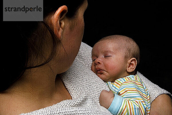Frau hält neugeborenes Kind  das sich an die Mutter kuschelt und friedlich schläft