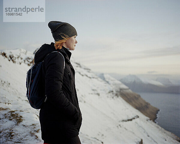 Frau steht auf einem verschneiten Berggipfel und blickt auf das Meer